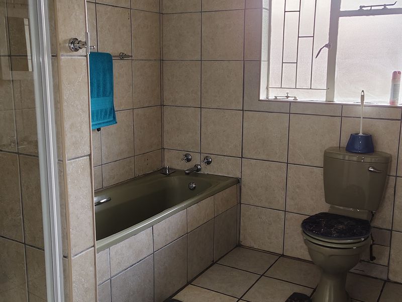A dated bathroom featuring tiled walls and flooring, a bathtub, a separate shower enclosure, and a pedestal basin.