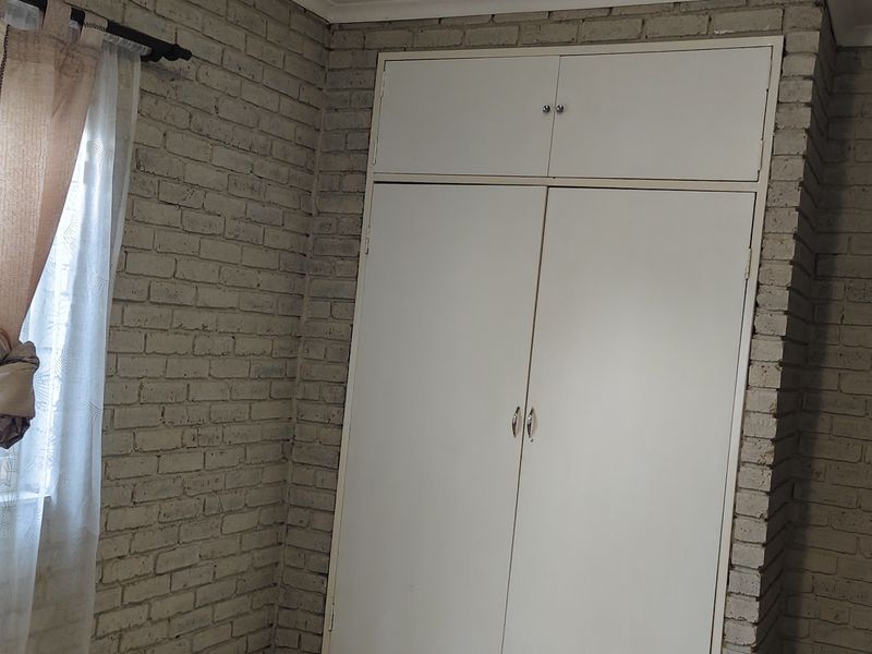 A bedroom featuring exposed brick walls and built-in storage cupboards with overhead cabinetry.