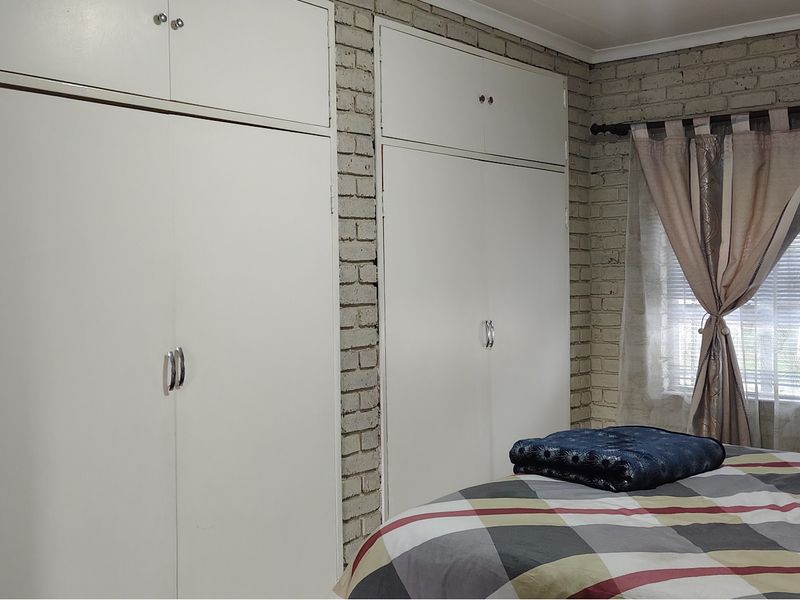 Bedroom featuring built-in cupboards and an exposed brick wall, providing a functional space with potential for modern updates.