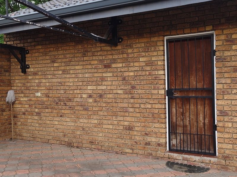 A paved outdoor patio area featuring face brick walls, a secure metal gate, and a metal awning structure.