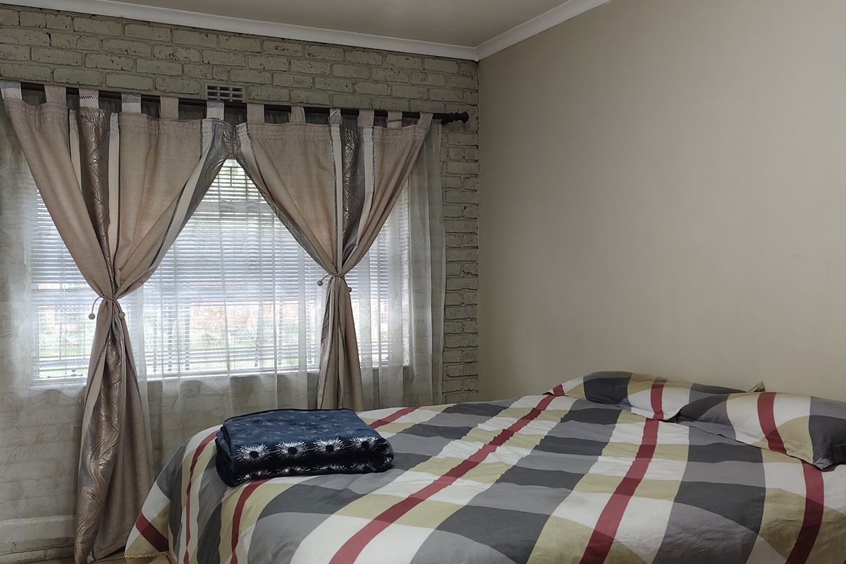 A bedroom featuring an exposed brick feature wall, built-in cupboards, and a window fitted with venetian blinds.