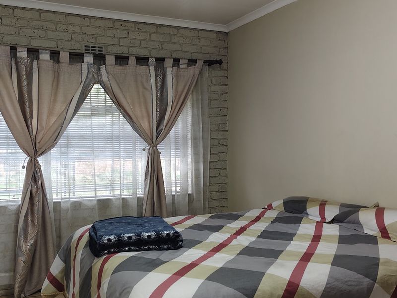 A bedroom featuring an exposed brick feature wall, built-in cupboards, and a window fitted with venetian blinds.