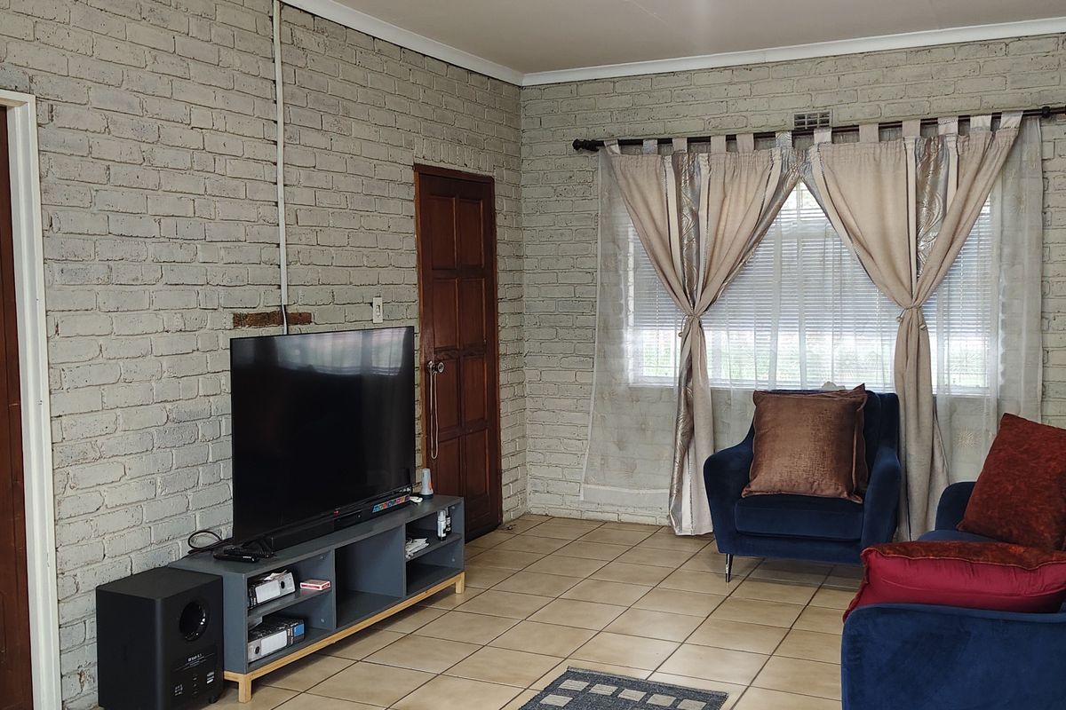 A living room featuring exposed brick walls, tiled flooring, and timber doors, offering a rustic aesthetic with potential for modern updates.