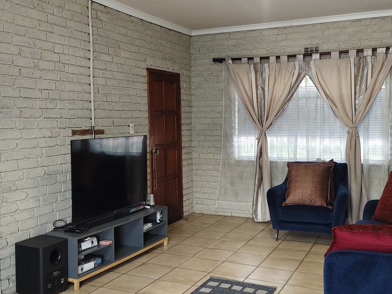 A living room featuring exposed brick walls, tiled flooring, and timber doors, offering a rustic aesthetic with potential for modern updates.