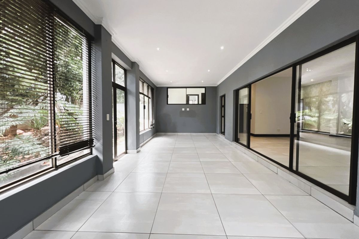 A spacious, light-filled living area featuring large glass sliding doors, modern tiled flooring, recessed ceiling lighting, and neutral grey wall finishes.
