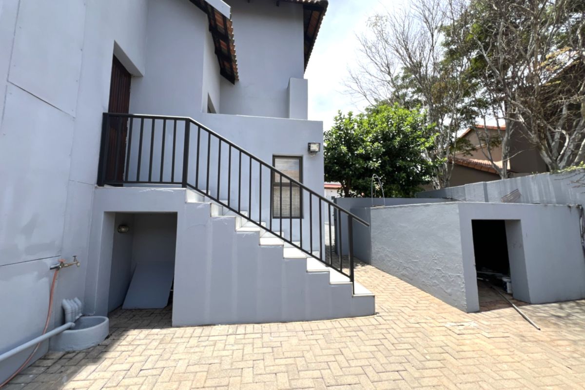 Rear exterior view of the property featuring a paved courtyard, external staircase with metal railing, and integrated storage alcoves.
