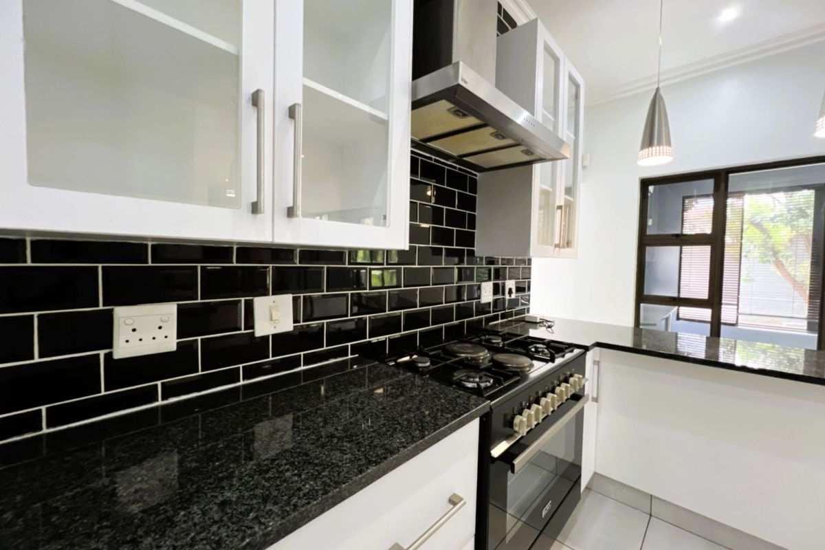 Modern kitchen featuring black granite countertops, white cabinetry, a gas hob with extractor fan, and a striking black subway tile backsplash.