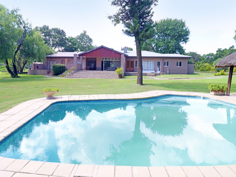 Spacious rear garden featuring a large swimming pool with paved surround, overlooking the main house with a raised patio area.