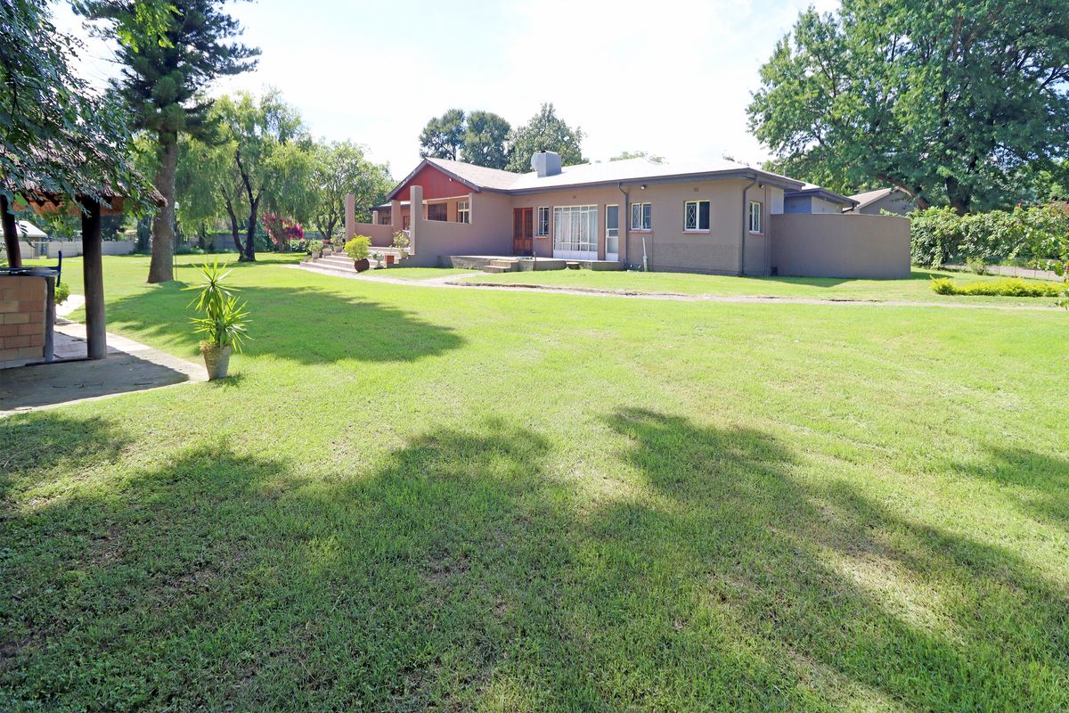 A spacious rear garden view featuring a large lawn, mature trees, and the rear elevation of the house with a covered patio area.