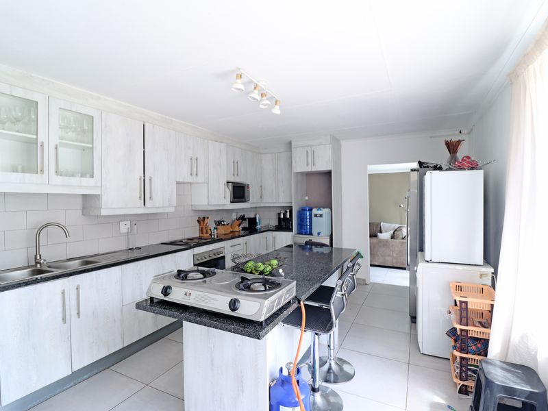A functional kitchen featuring white cabinetry, dark granite countertops, a central island with a gas hob, and tiled flooring.