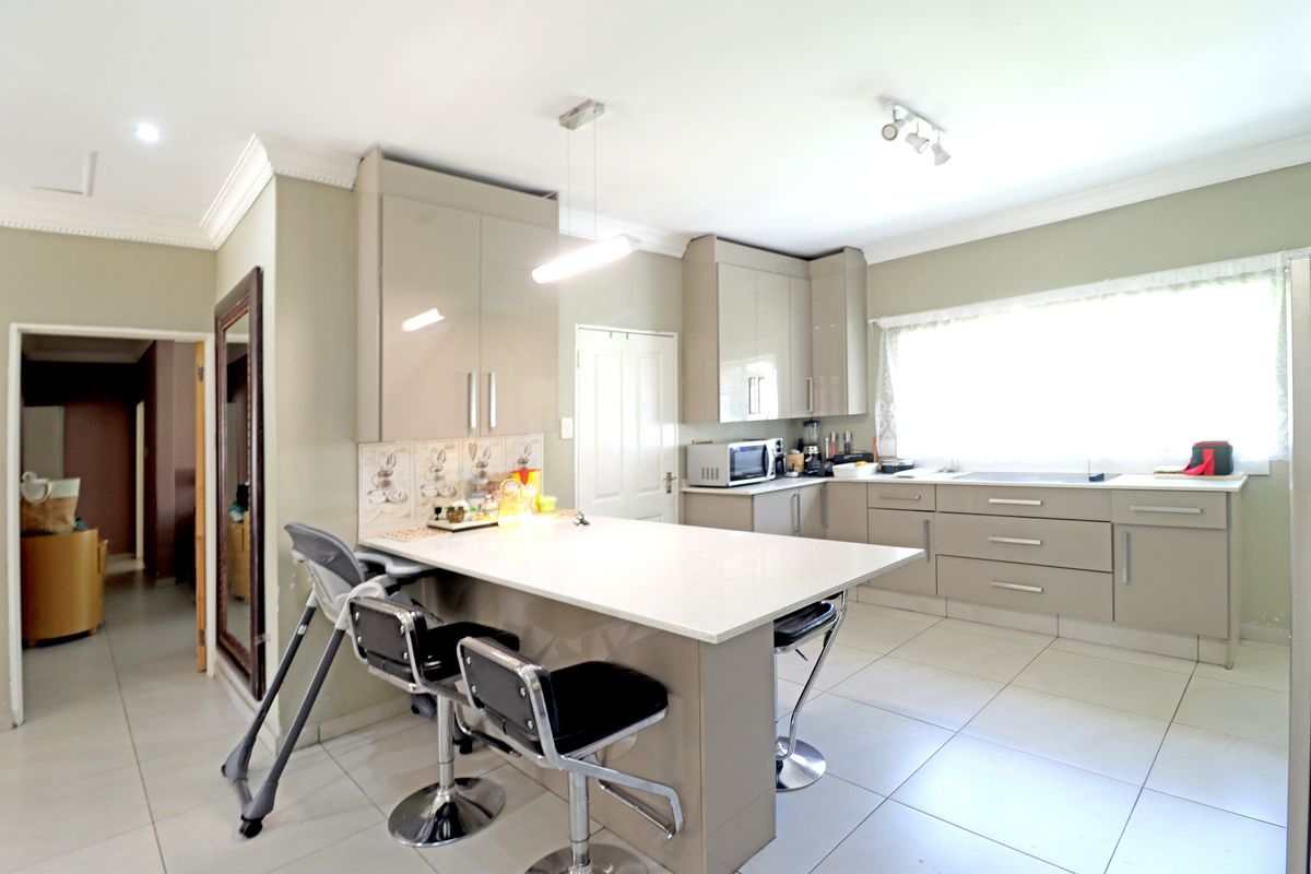 Modern kitchen featuring high-gloss cabinetry, stone countertops, a central breakfast island, and tiled flooring.