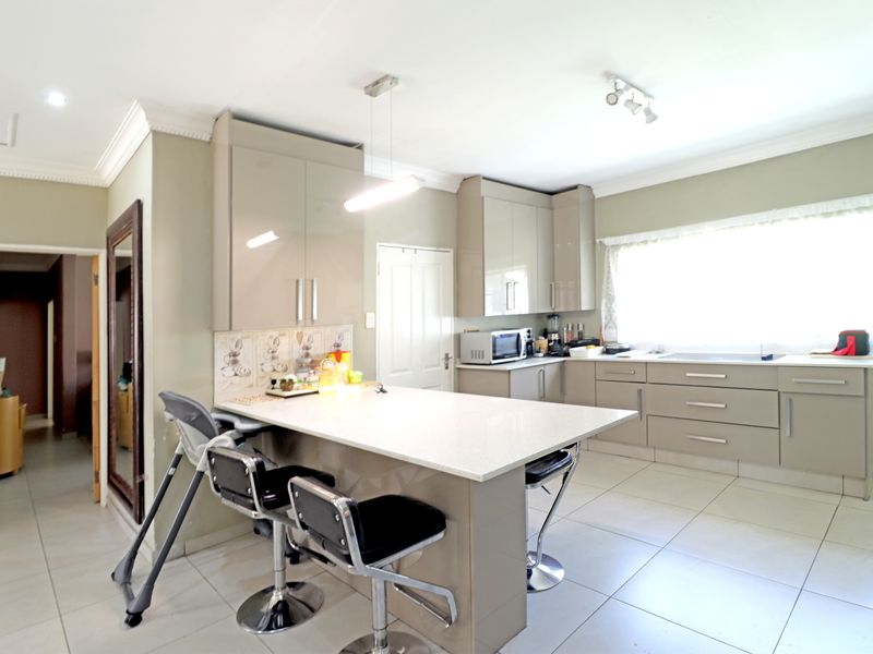 Modern kitchen featuring high-gloss cabinetry, stone countertops, a central breakfast island, and tiled flooring.