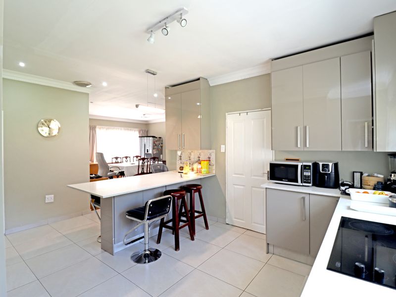 Modern kitchen featuring sleek cabinetry, a breakfast bar, and tiled flooring, seamlessly flowing into the adjacent dining area.