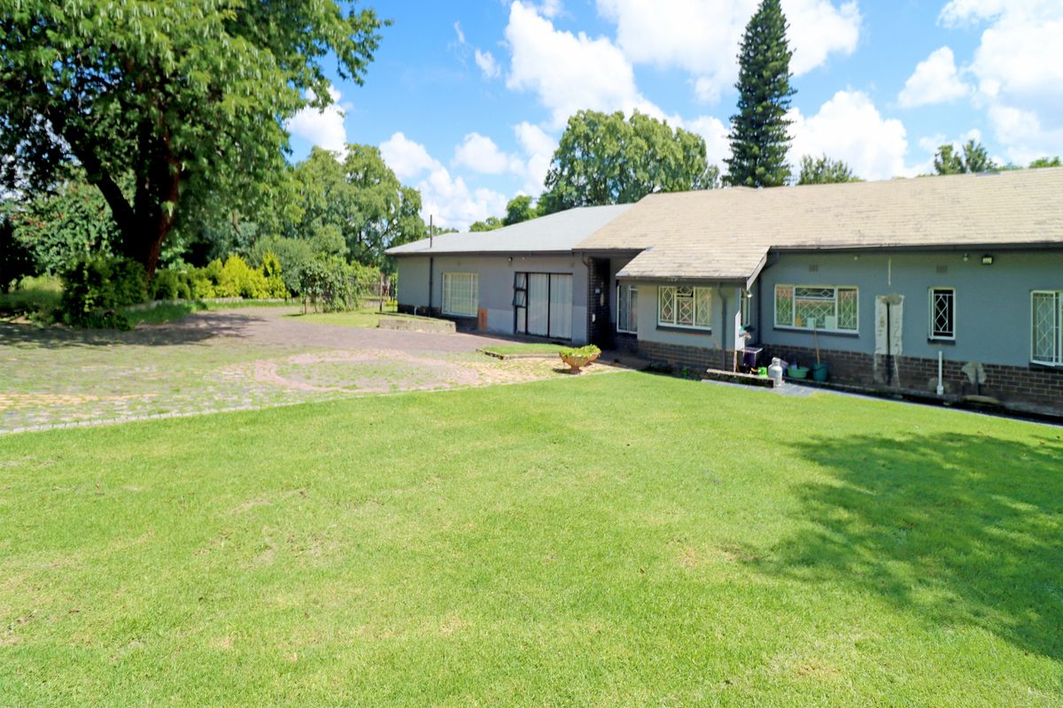 A view of the rear exterior of the house, featuring a large lawn, paved area, and established garden surroundings.