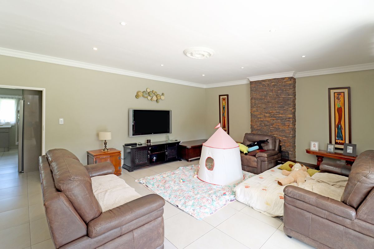 Spacious living room featuring tiled flooring, recessed downlighting, decorative ceiling rose, and a prominent stone-clad feature wall.