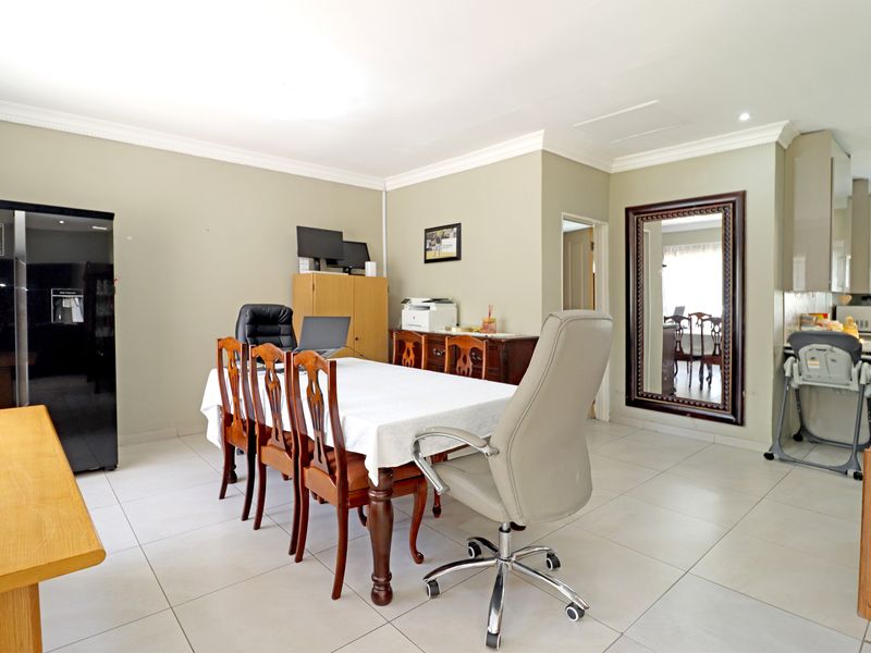 Open plan living and dining area featuring neutral wall tones, tiled flooring, and crown molding, with a partial view into the kitchen area.