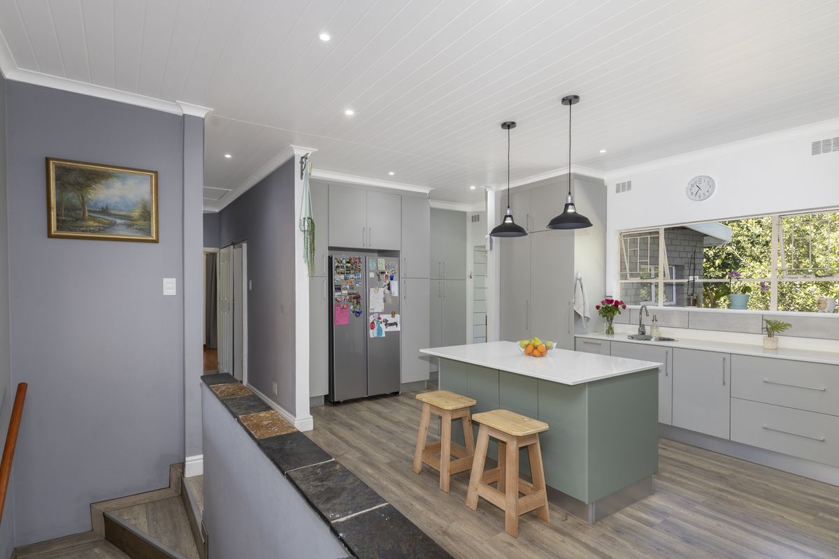 Modern kitchen featuring a central island, stone countertops, sleek grey cabinetry, and recessed lighting, seamlessly integrated with the home's open-plan layout.