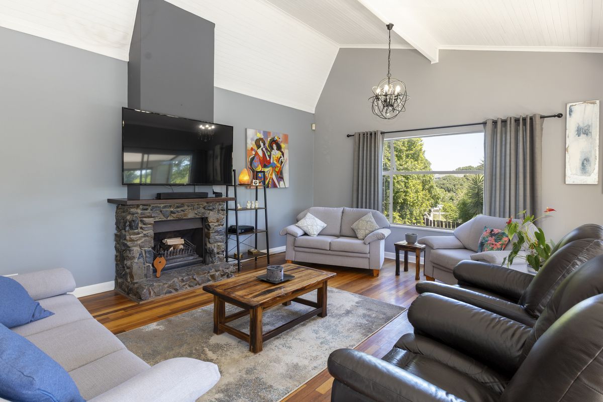 Spacious living room featuring a stone fireplace, vaulted ceilings with exposed beams, and polished timber flooring, offering a warm and inviting atmosphere.
