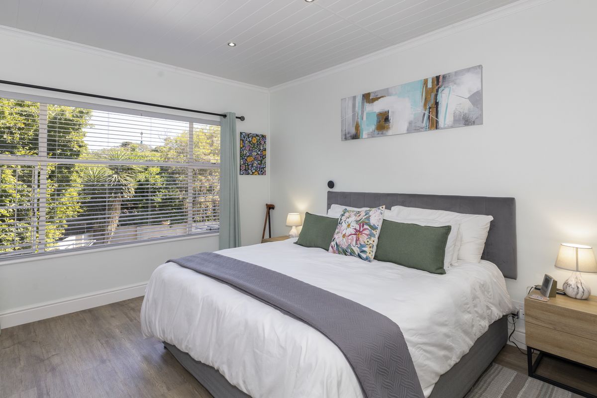 A bright and well-maintained bedroom featuring laminate flooring, recessed downlighting, and a large window with venetian blinds overlooking the garden.
