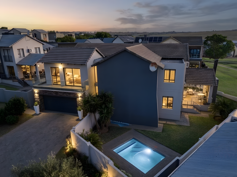 Aerial view of a modern double-story residential property featuring a swimming pool, paved driveway, and balcony at twilight.