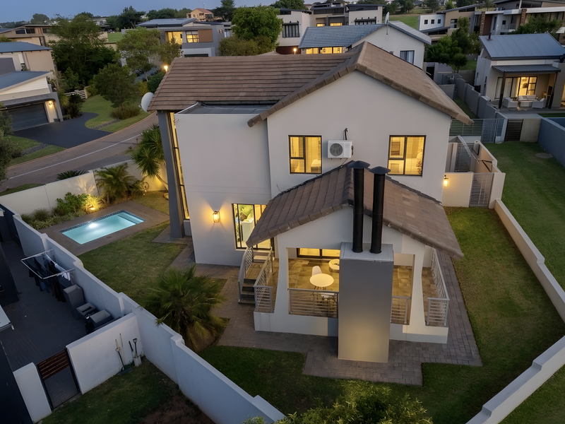 Aerial view of a modern two-story residential property featuring a tiled roof, private swimming pool, covered patio with an outdoor fireplace, and landscaped garden.