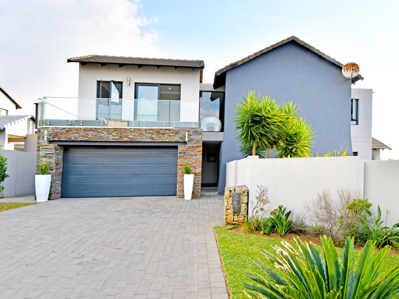 Modern double-storey home featuring a paved driveway, double garage, stone-clad facade, and an upper-level balcony with a glass balustrade.