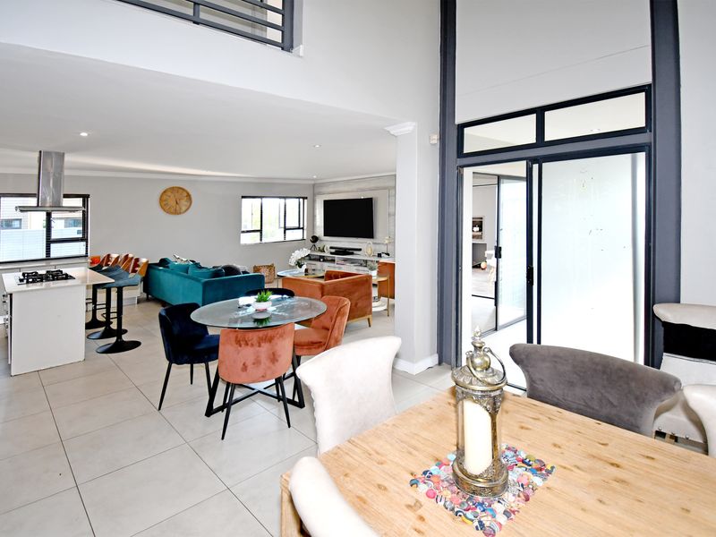 Spacious open-plan living area featuring a modern kitchen with island, double-volume ceilings, and seamless flow to the outdoor patio through large sliding doors.