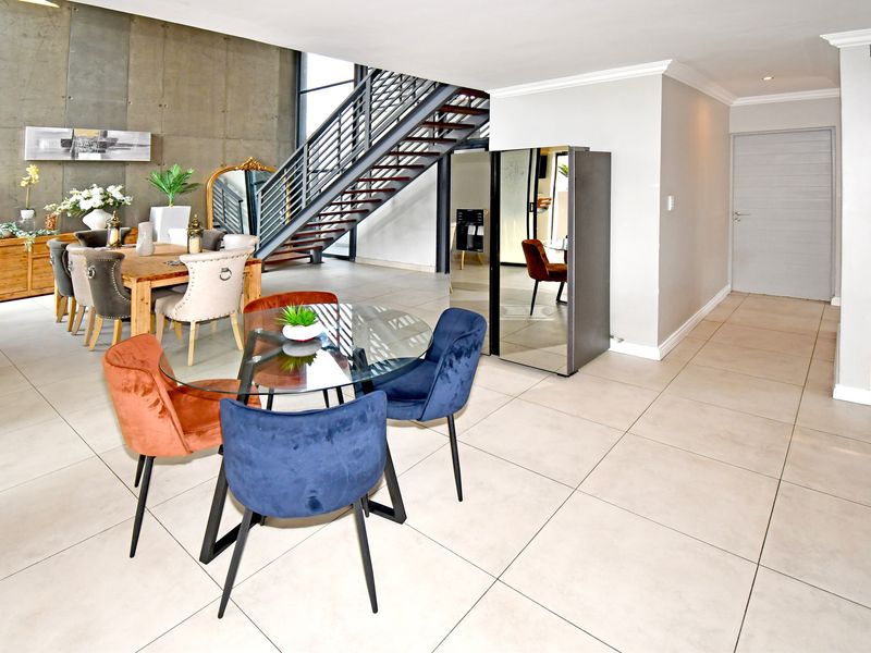 Spacious open-plan living area featuring an industrial-style exposed concrete wall, a modern metal staircase, and large format floor tiles.