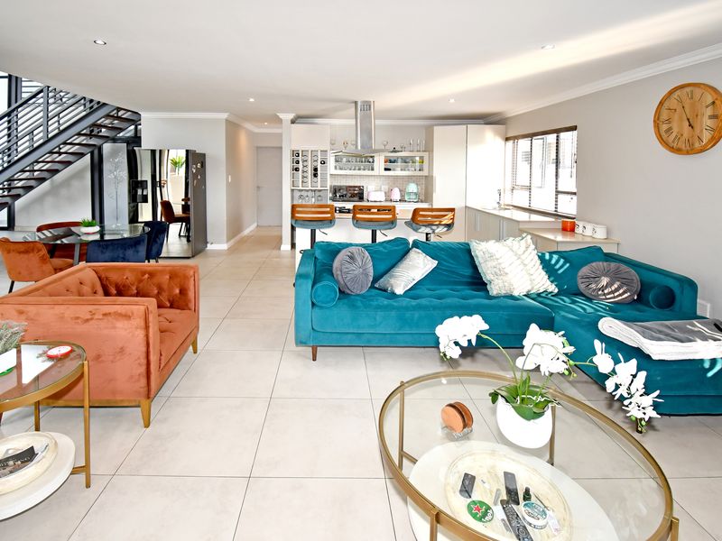 Spacious open-plan living area featuring a modern kitchen with island, tiled floors, and a contemporary staircase leading to the upper level.