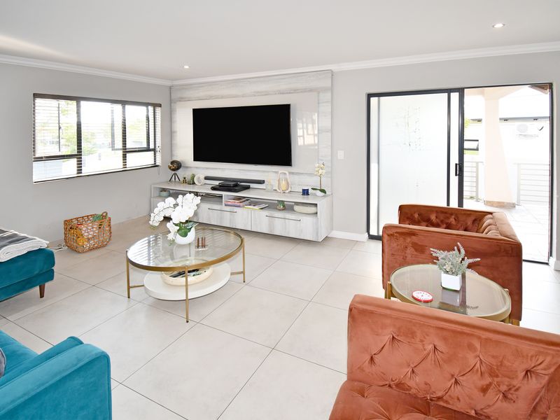 A bright and modern living room featuring large format floor tiles, recessed lighting, and a custom built-in media wall with direct access to the patio.