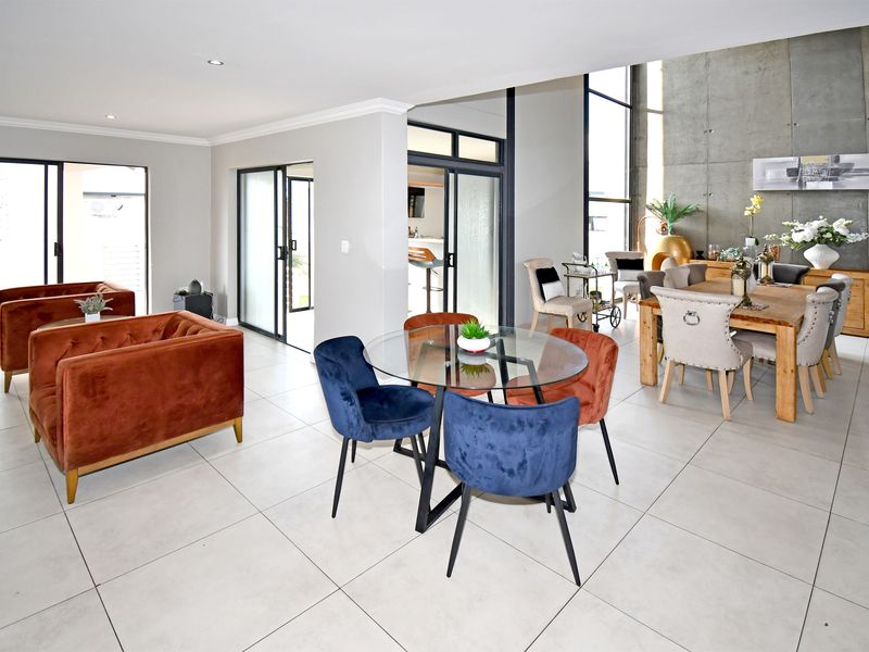 Spacious open-plan living and dining area featuring large sliding glass doors, tiled flooring, and a striking exposed concrete feature wall.