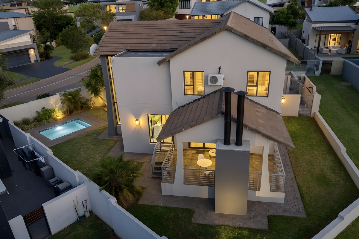 Aerial view of a modern two-story residential property featuring a tiled roof, private swimming pool, covered patio with an outdoor fireplace, and landscaped garden.