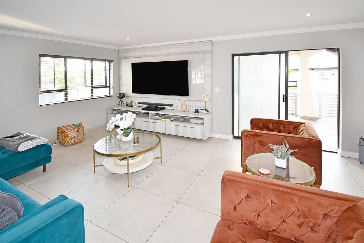 A bright and modern living room featuring large format floor tiles, recessed lighting, and a custom built-in media wall with direct access to the patio.