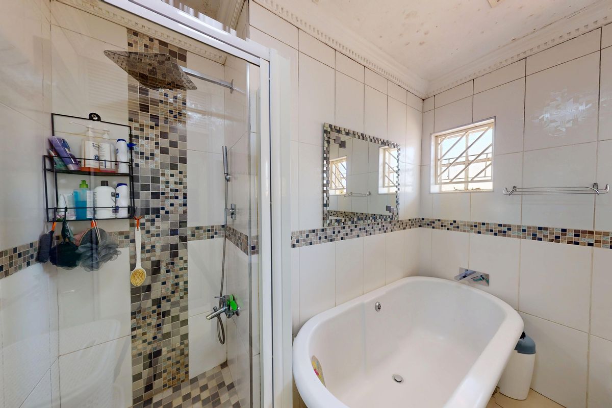 A bathroom featuring a shower enclosure, a freestanding bathtub, and mosaic tile detailing. Note visible water staining on the ceiling.