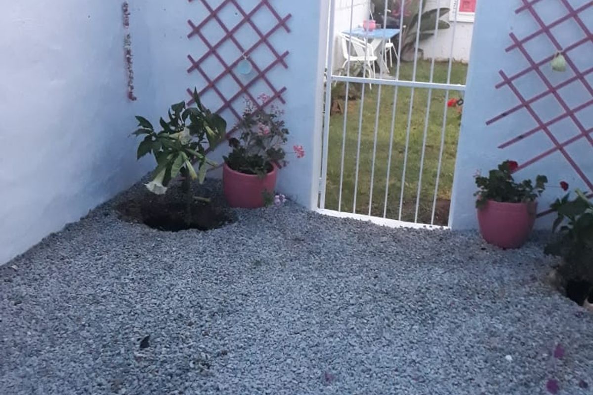 A small rear courtyard area featuring gravel ground cover, decorative wooden lattice wall panels, and a metal security gate leading to the garden.