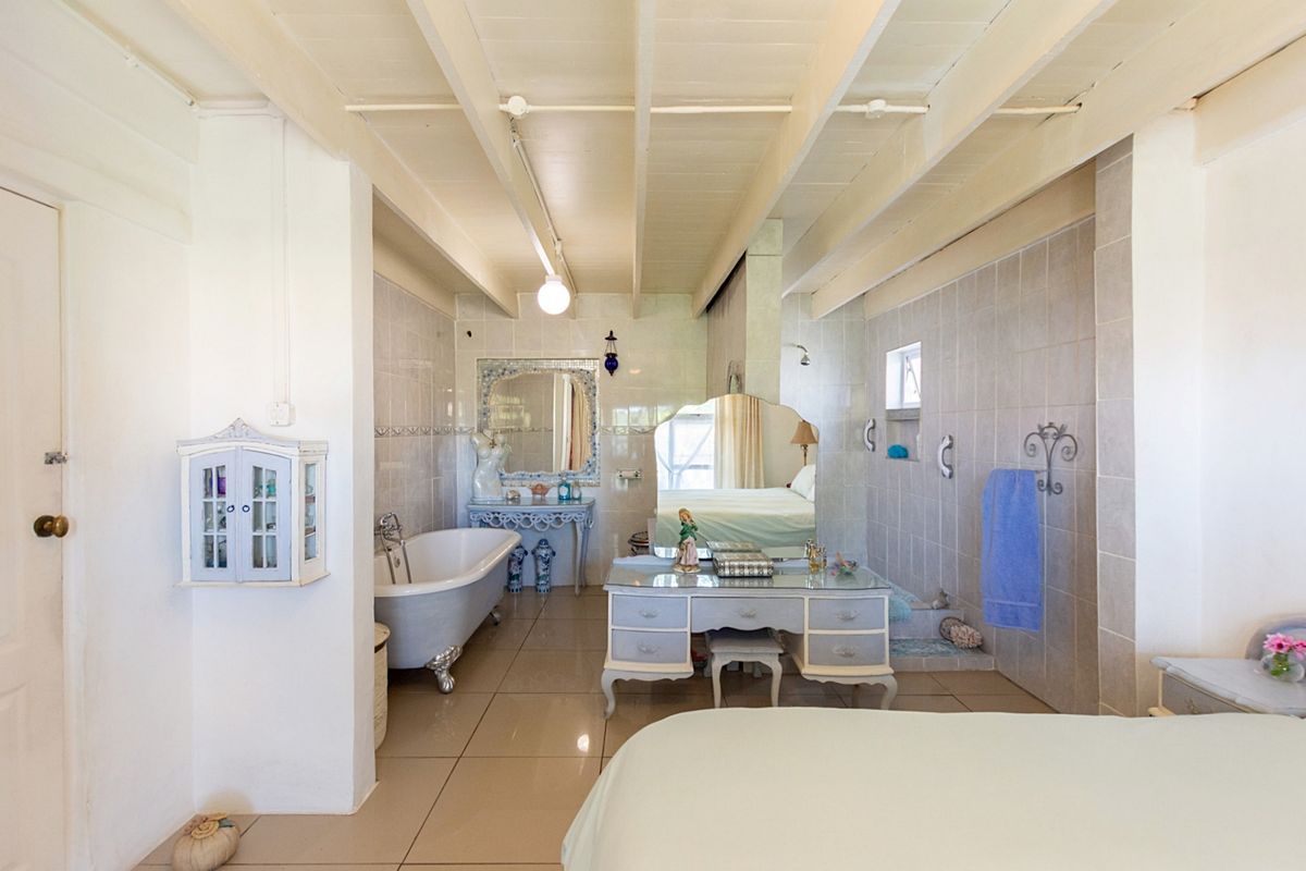 A spacious bedroom featuring an integrated clawfoot bathtub, tiled flooring, and exposed beam ceilings, creating a unique open-concept ensuite layout.