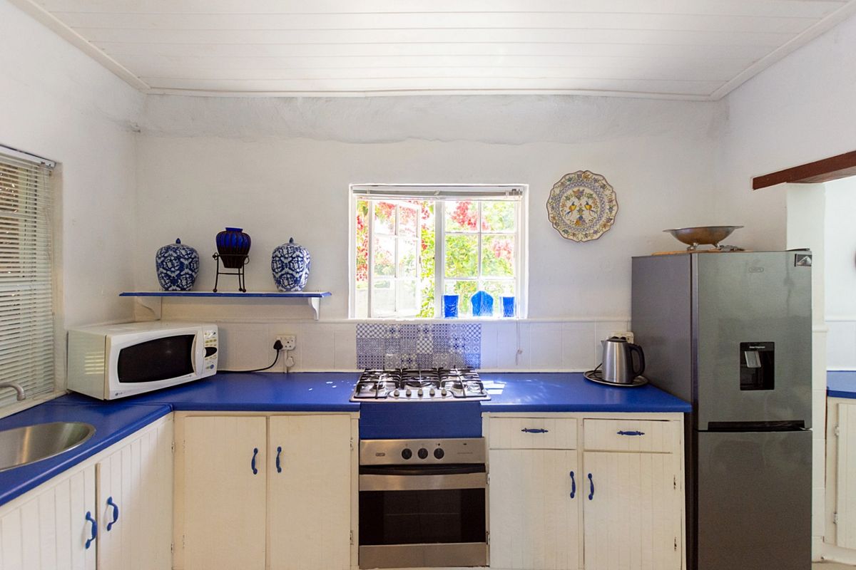 A functional kitchen featuring blue countertops, white cabinetry, a gas hob, built-in oven, and a window overlooking the garden.