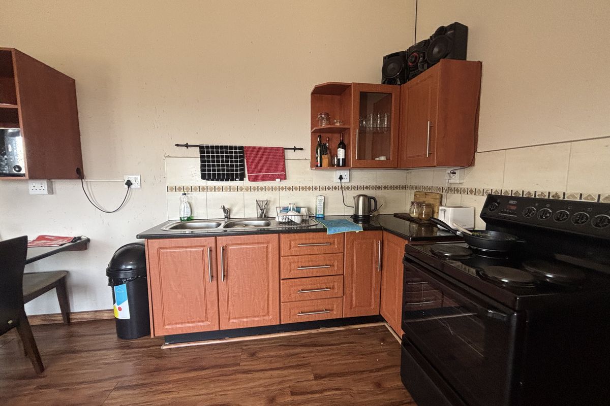 Functional kitchen featuring wood-finish cabinetry, laminate countertops, double basin sink, and a freestanding electric stove with oven.