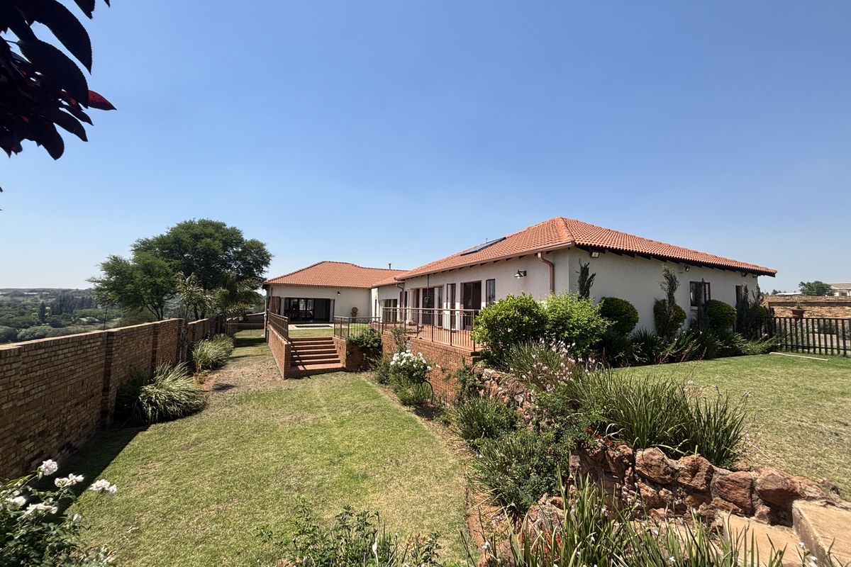 A view of the rear exterior of the house, featuring a landscaped garden, brick boundary walls, and a raised patio area with stairs.