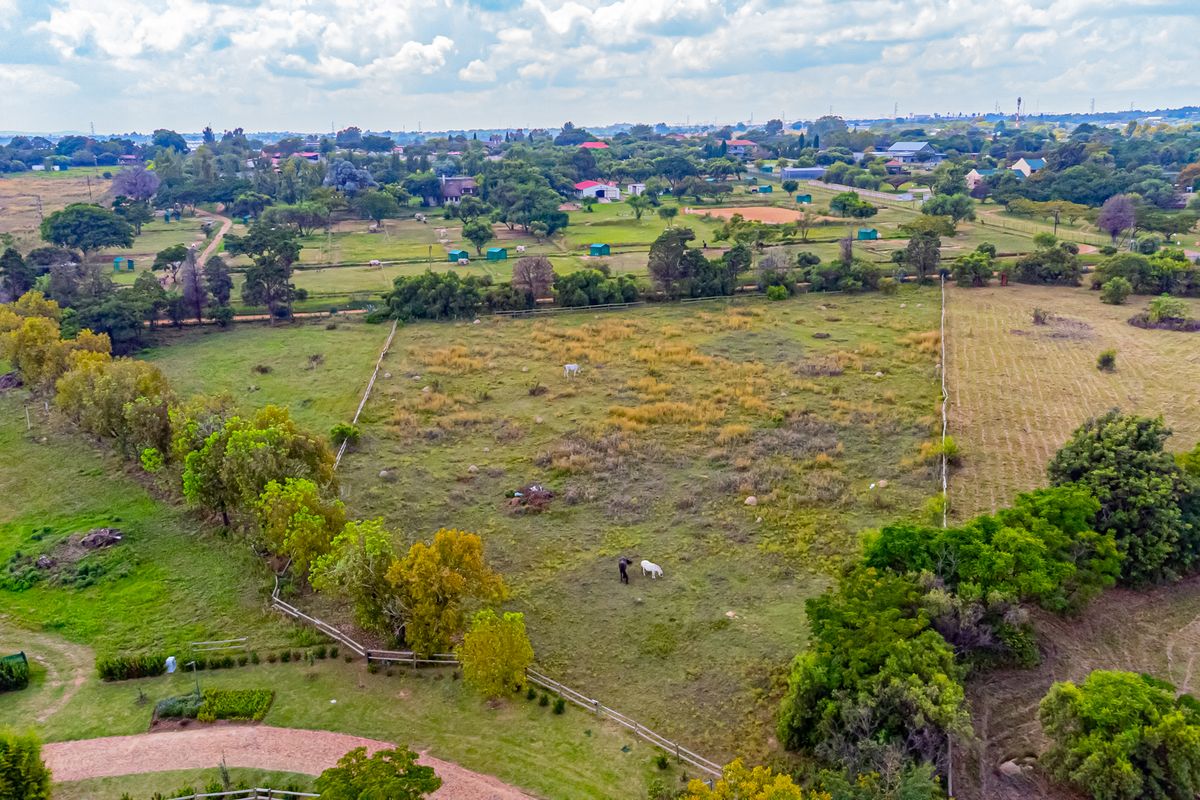 An aerial view of a large, open residential vacant land plot featuring established trees and perimeter fencing in a semi-rural setting.