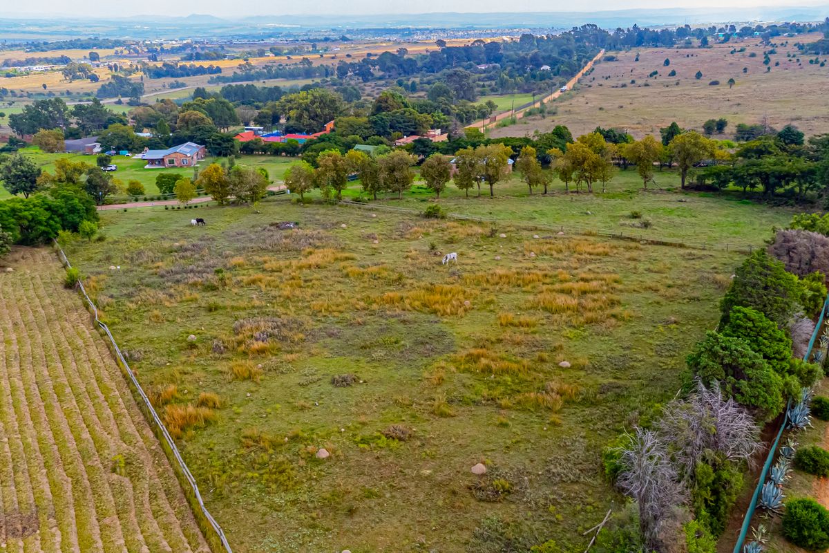 Aerial view of a large, open residential vacant land plot featuring natural grass cover, perimeter fencing, and adjacent dirt road access.