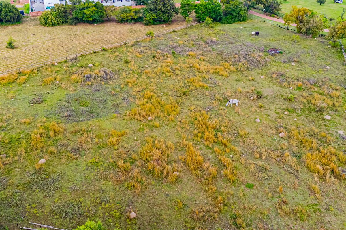 An aerial view of a vacant residential plot featuring open grassland and perimeter fencing, suitable for future development.