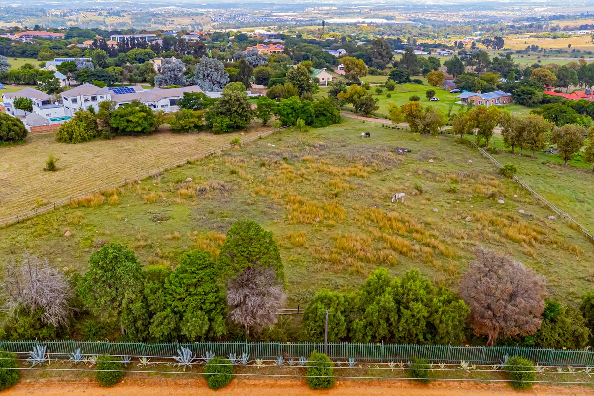 An aerial view of a large, vacant residential plot featuring established trees, perimeter fencing, and surrounding neighborhood views.
