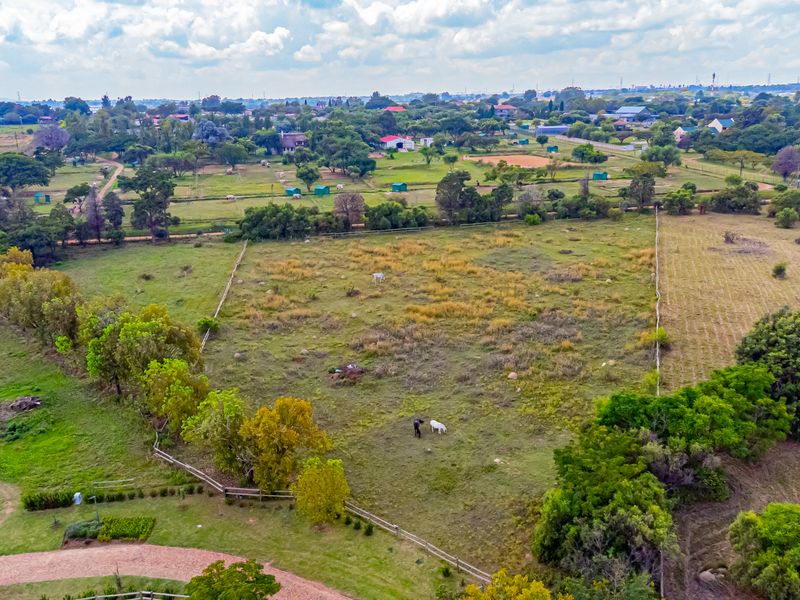An aerial view of a large, open residential vacant land plot featuring established trees and perimeter fencing in a semi-rural setting.