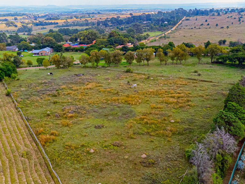Aerial view of a large, open residential vacant land plot featuring natural grass cover, perimeter fencing, and adjacent dirt road access.