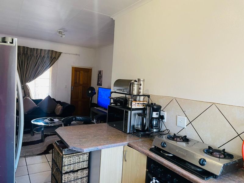 Open-plan living area featuring a compact kitchen with gas hob, tiled backsplash, and tiled flooring, flowing into a connected lounge space.