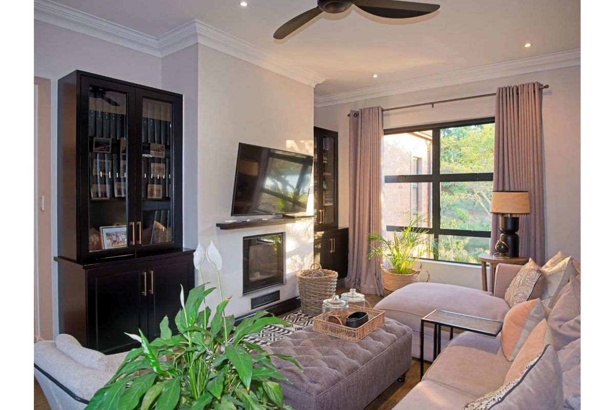 A well-appointed living room featuring built-in cabinetry, a modern fireplace, crown molding, and a large window providing natural light and garden views.