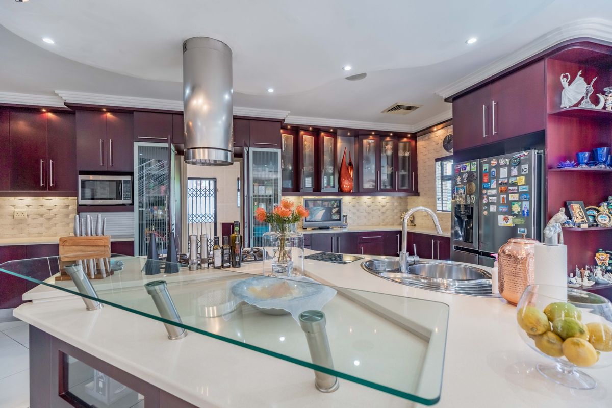 A spacious kitchen featuring dark cabinetry, a large island with a glass breakfast bar, stone countertops, and integrated stainless steel appliances.