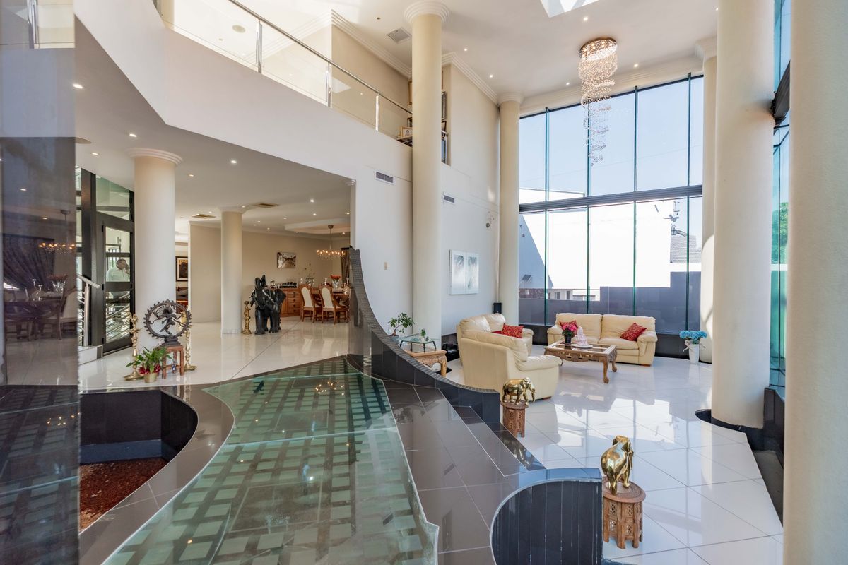 Spacious double-volume living area featuring floor-to-ceiling windows, polished tile flooring, structural columns, and a unique indoor water feature.