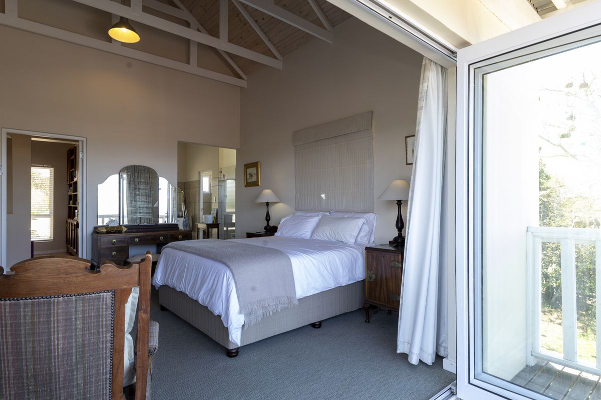 Spacious bedroom featuring a high vaulted ceiling with exposed timber trusses, neutral finishes, and direct access to a private balcony through double glass doors.
